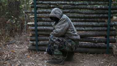 Person with hooded jacket in front of logged cabin.